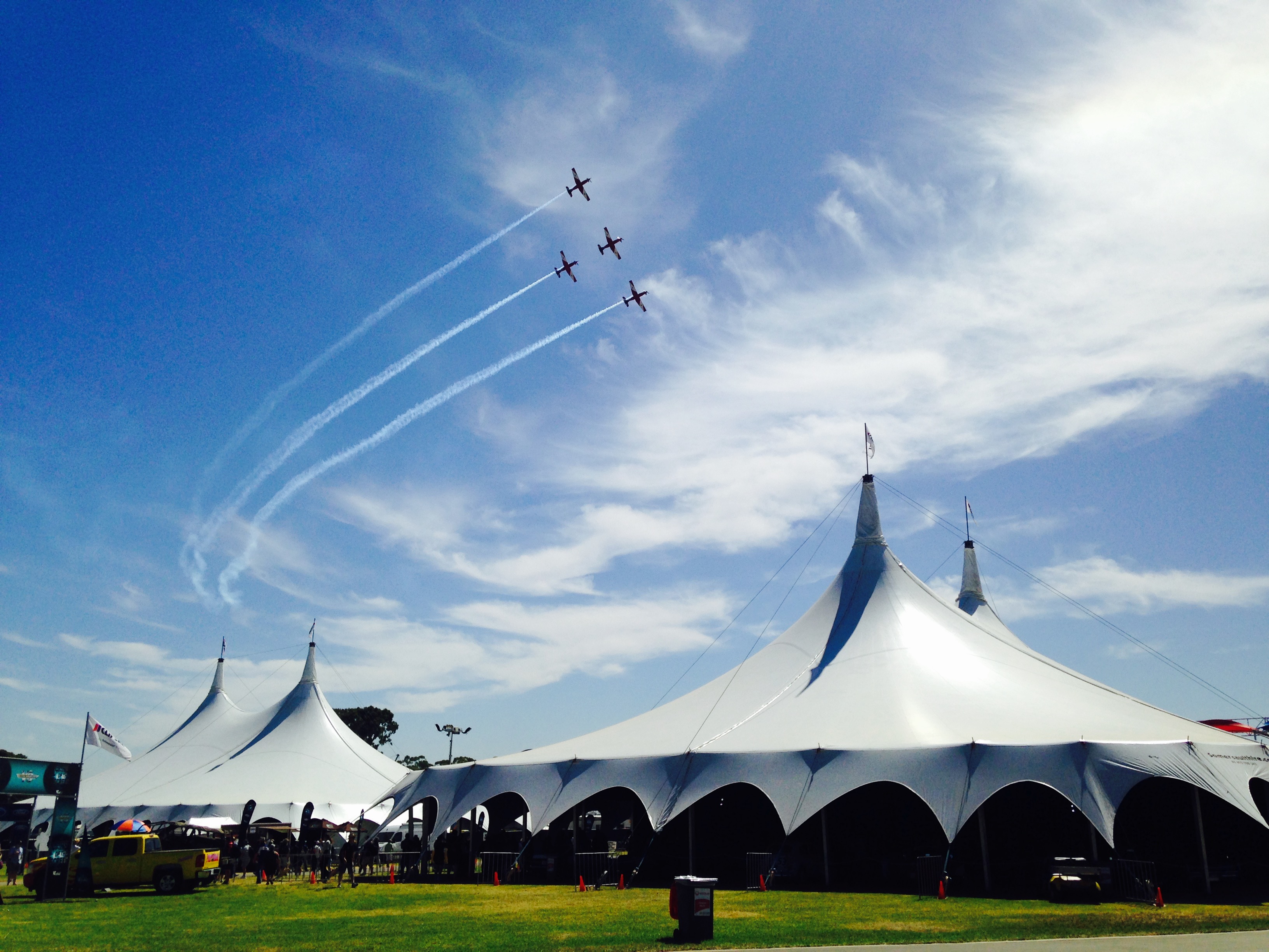 Two Somersault peak-pole structures on an airshow site, with a formation of aircraft trailing smoke overhead